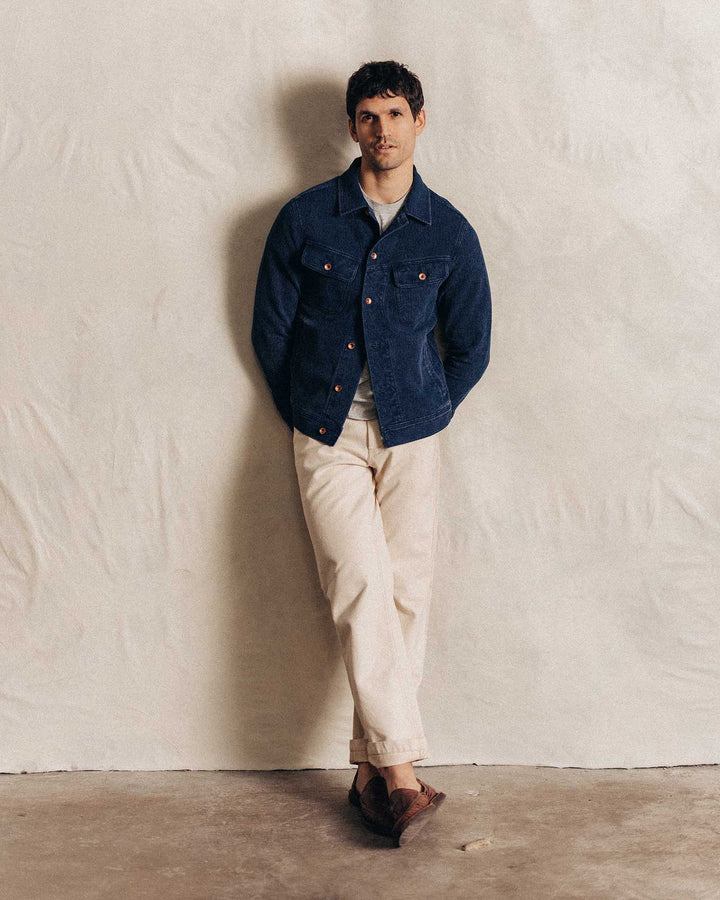 man wearing jean jacket and white pants against a white wall.