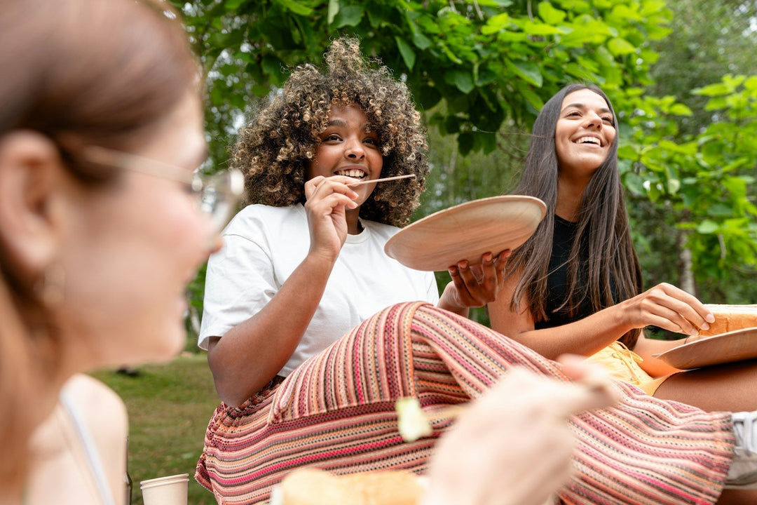 a group of three smiling women having a picnic in a park in summertime