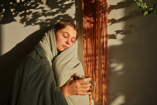 A person with a blanket wrapped around them standing inside in the afternoon light