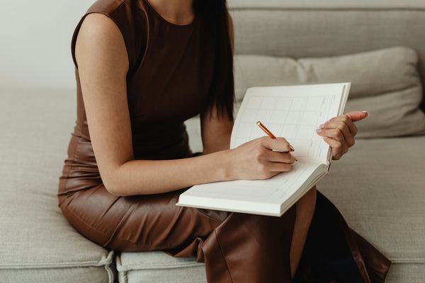 A woman wearing a brown dress writing in a calendar or planner