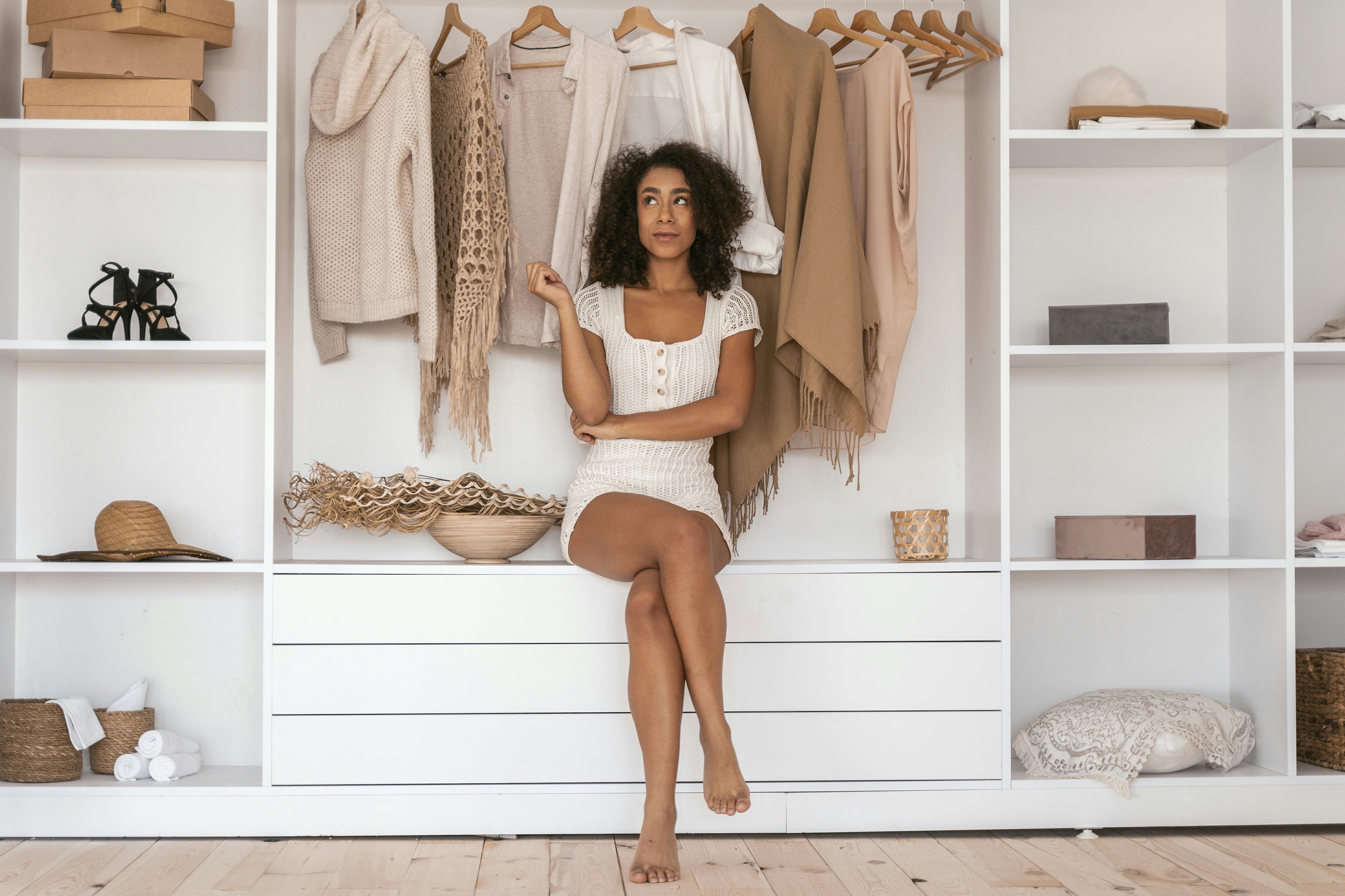 A woman wearing a crochet romper sitting in her closet looking contemplative