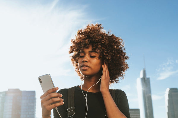 A person looking at their phone while wearing headphones with a city skyline in the background