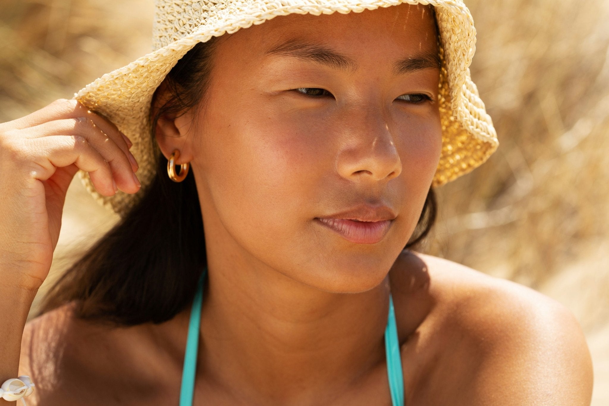 A woman looking away from the camera, wearing a sun hat and blue bikini top