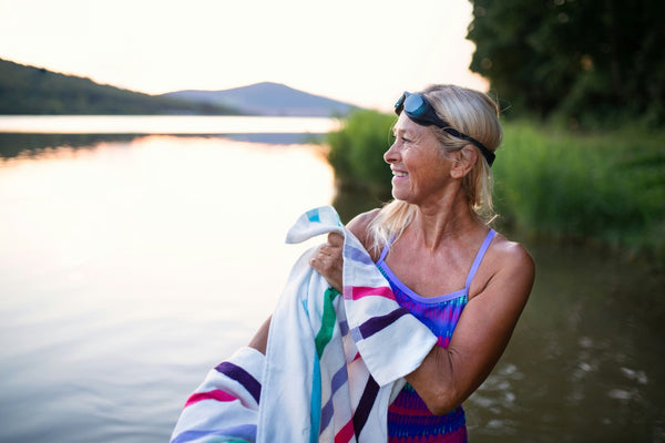 A mature woman smiling, wearing a bathing suit and swimming goggles, standing in a river at golden hour
