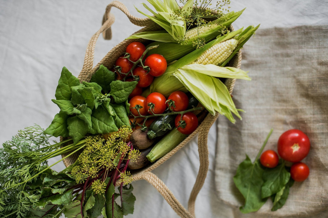 A jute tote filled with fresh produce set atop a linen tablecloth