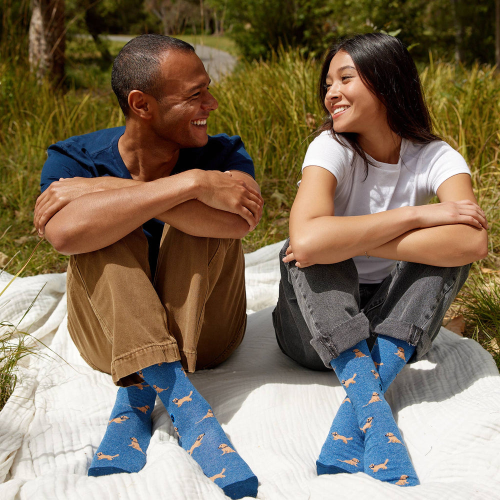 Two people sitting on a blanket outdoors wearing blue socks with dog patterns.