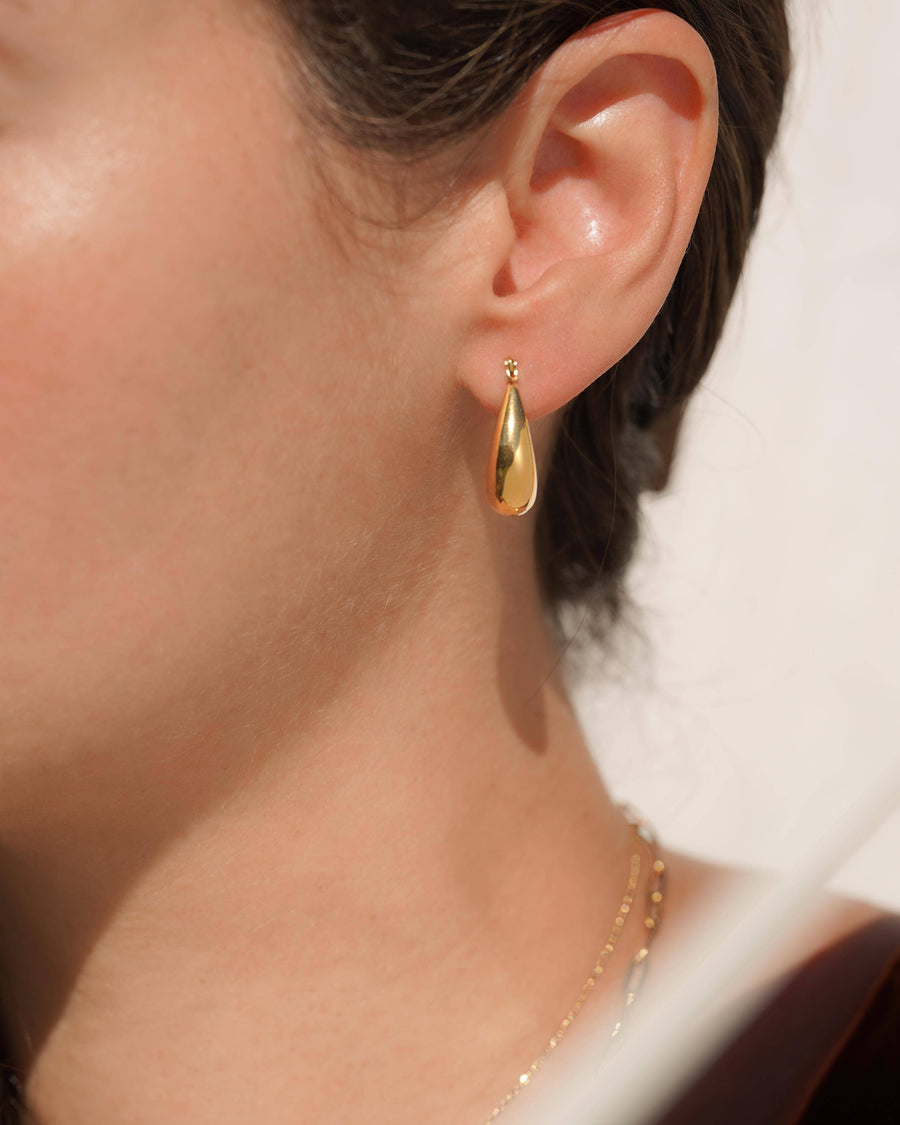 Gold teardrop earring worn by a person with a blurred background