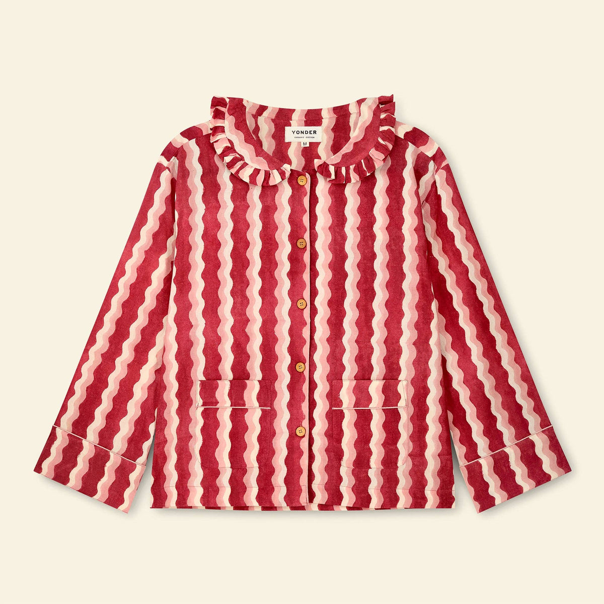 A long-sleeve button-front top with a ruffled collar and vertical wavy stripes in red and cream, shown flat against a light beige background. A neck label reads YONDER.