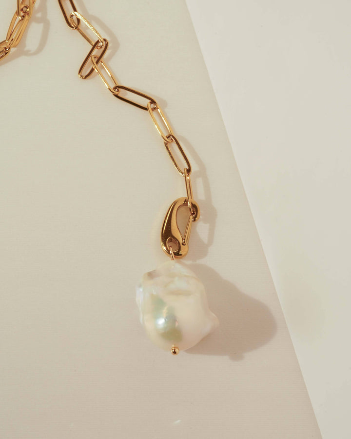 Gold chain necklace with a pearl pendant on a light background