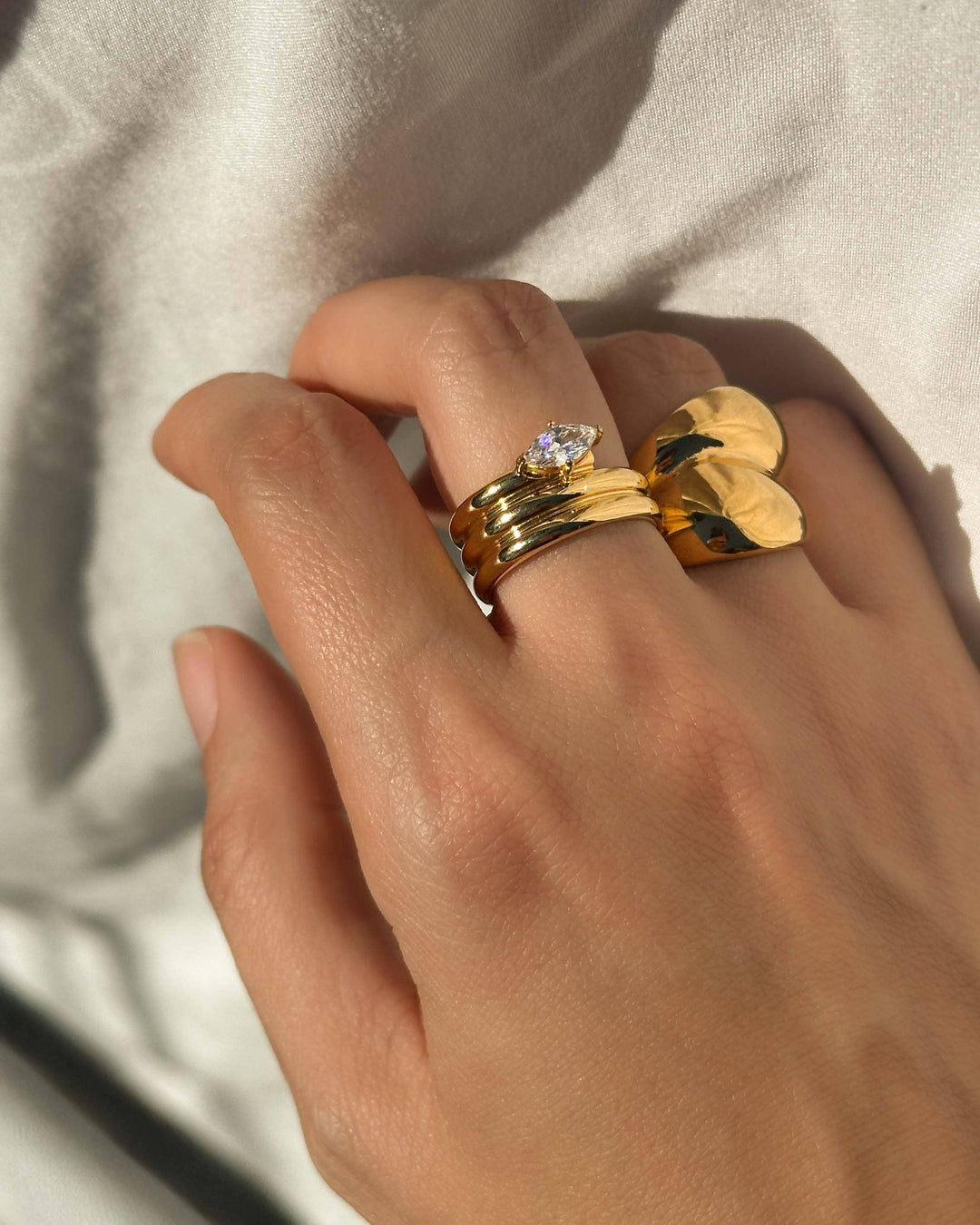 Hand wearing multiple gold rings with a light background