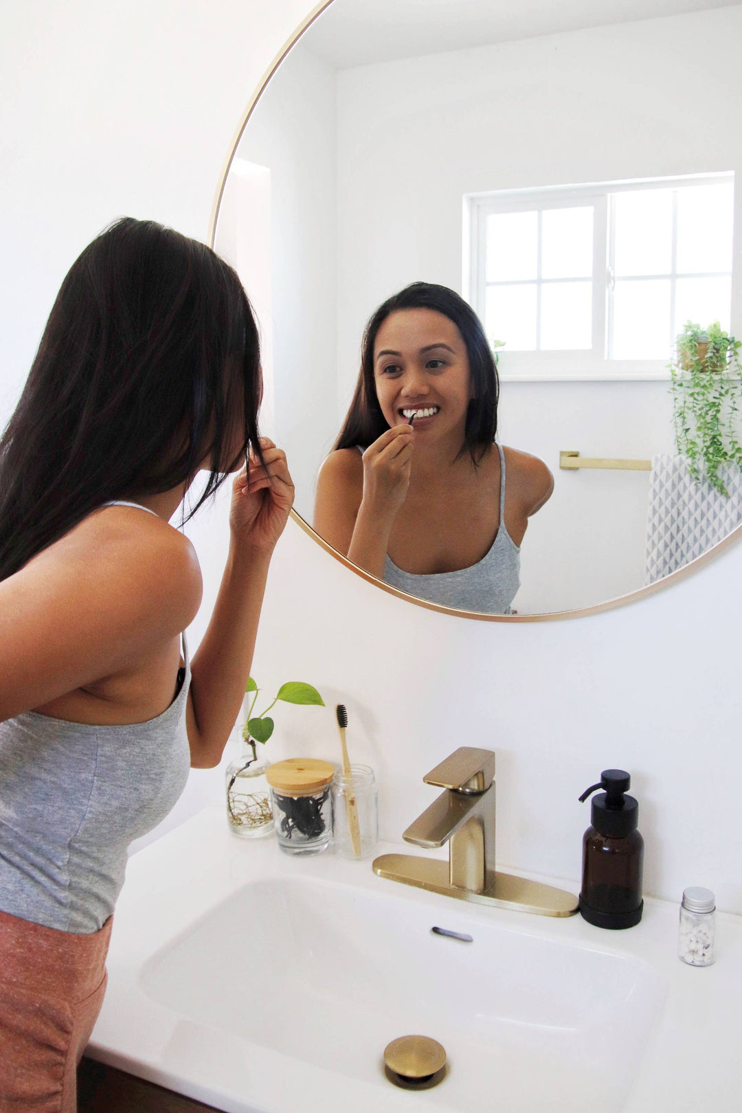 A woman using dental floss pick in front of a round mirror in a bathroom.