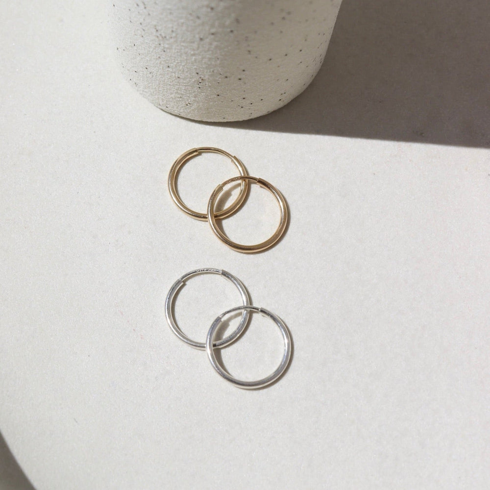 Two pairs of hoop earrings, one gold and one silver, on a light surface with a neutral background.