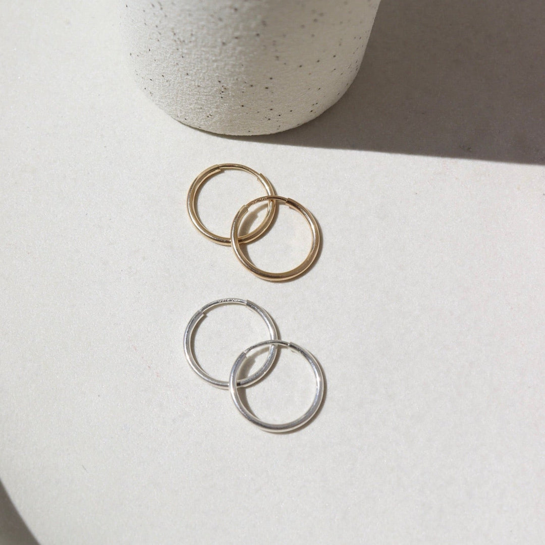 Two pairs of hoop earrings, one gold and one silver, on a light surface with a neutral background.