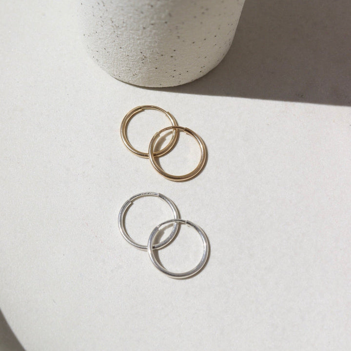Two pairs of hoop earrings, one gold and one silver, on a light surface with a neutral background.
