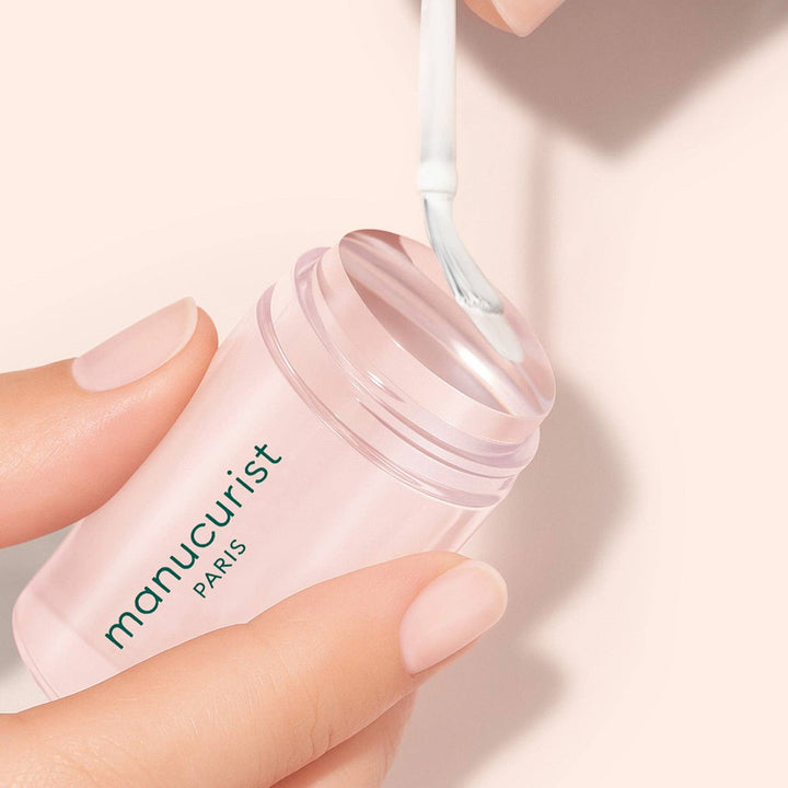 Hand holding a 'manucurist' nail stamper with a light pink background