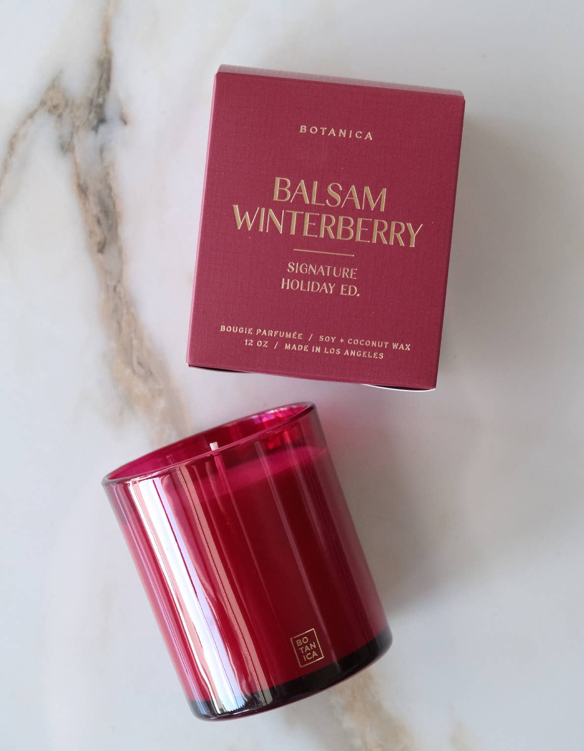 Red candle and box labeled 'Balsam Winterberry' on a marble surface