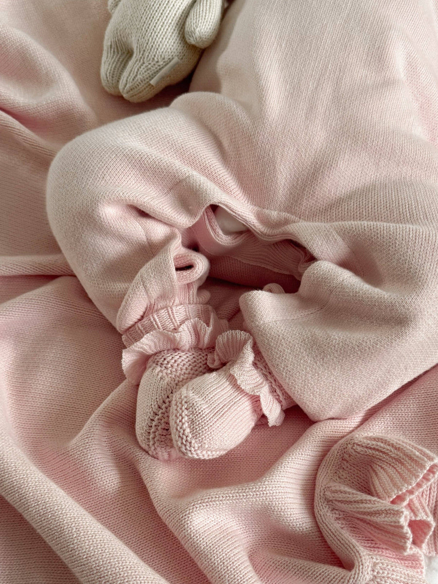 Close-up of pink baby clothing and matching booties on a soft pink fabric background