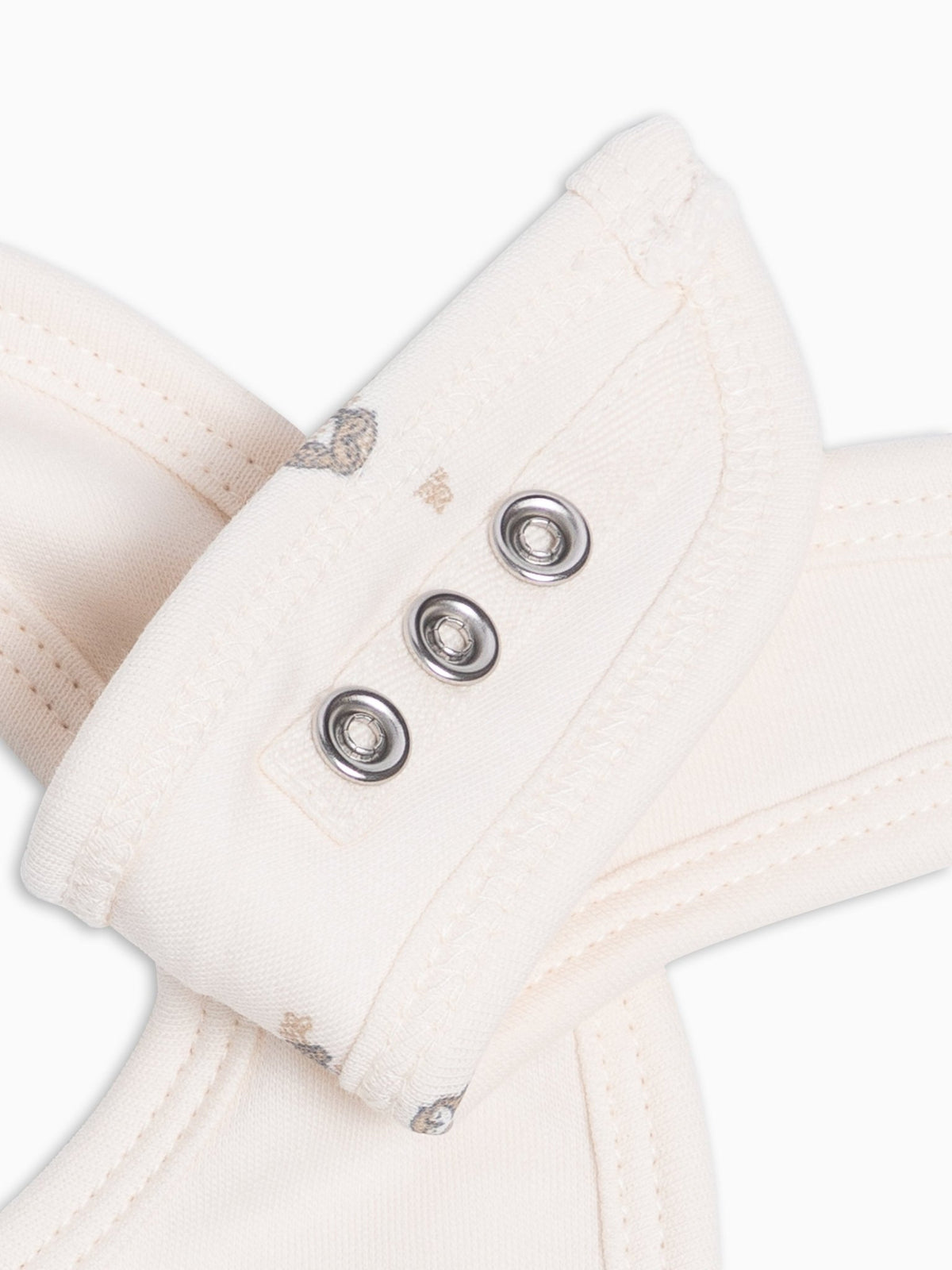 Close-up of a cream-colored fabric accessory with three silver metal snap buttons on a white background.