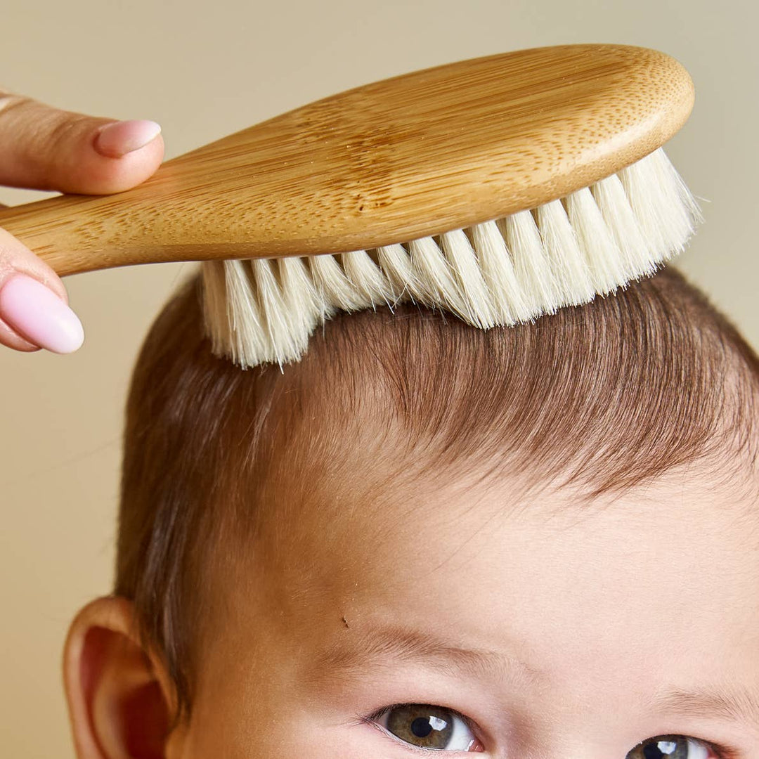 Person using a wooden brush on a child's head against a beige background