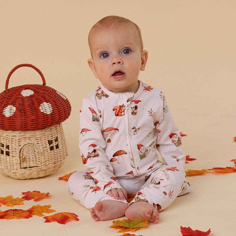Baby wearing a Gnomes Organic Snugglesuit Convertible Romper, sitting next to a wicker basket with a red top on a beige background.