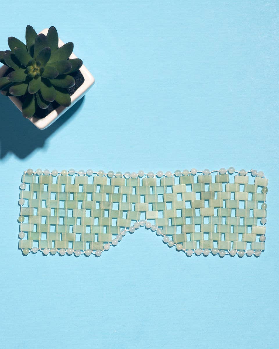 Green woven eye mask on a blue background with a small potted plant.