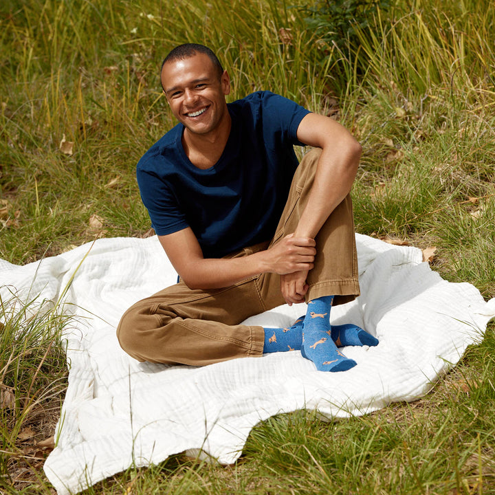 Man sitting on a white blanket in a grassy area wearing blue socks with a dog pattern.