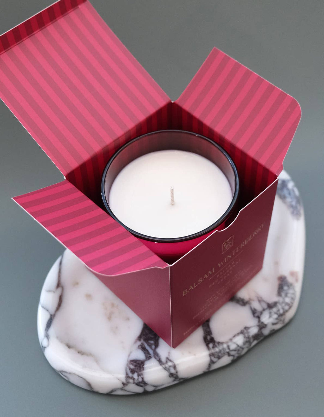 Candle in a red box on a marble coaster with a gray background