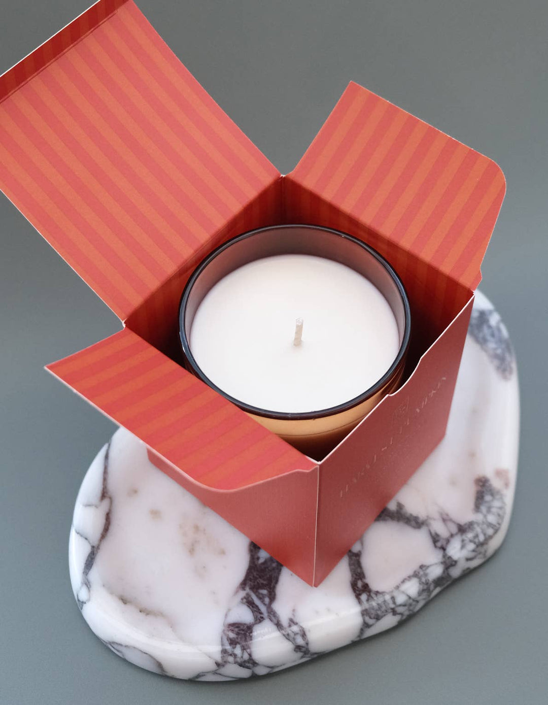 Candle in a orange box on a marble coaster with a gray background