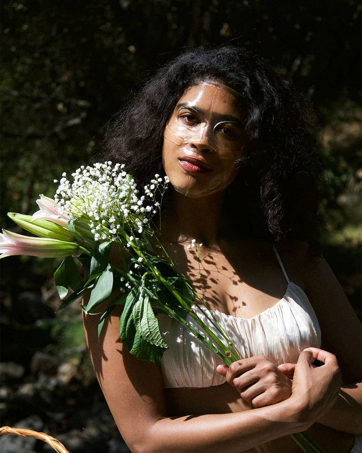 Woman holding a bouquet of flowers wearing a face mask in a natural setting