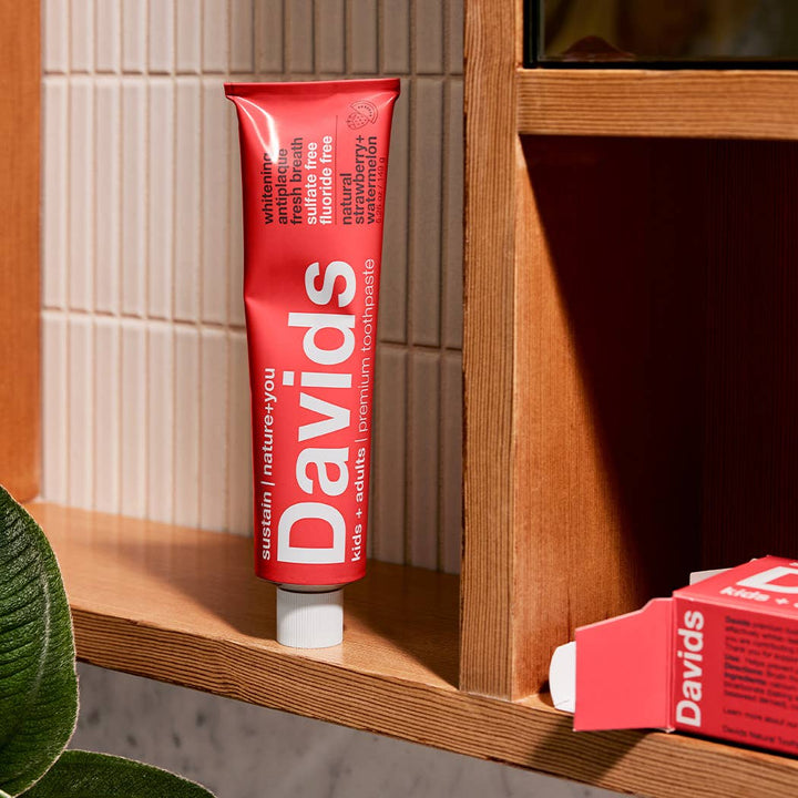 Red Davids toothpaste tube on a wooden shelf with a box next to it.