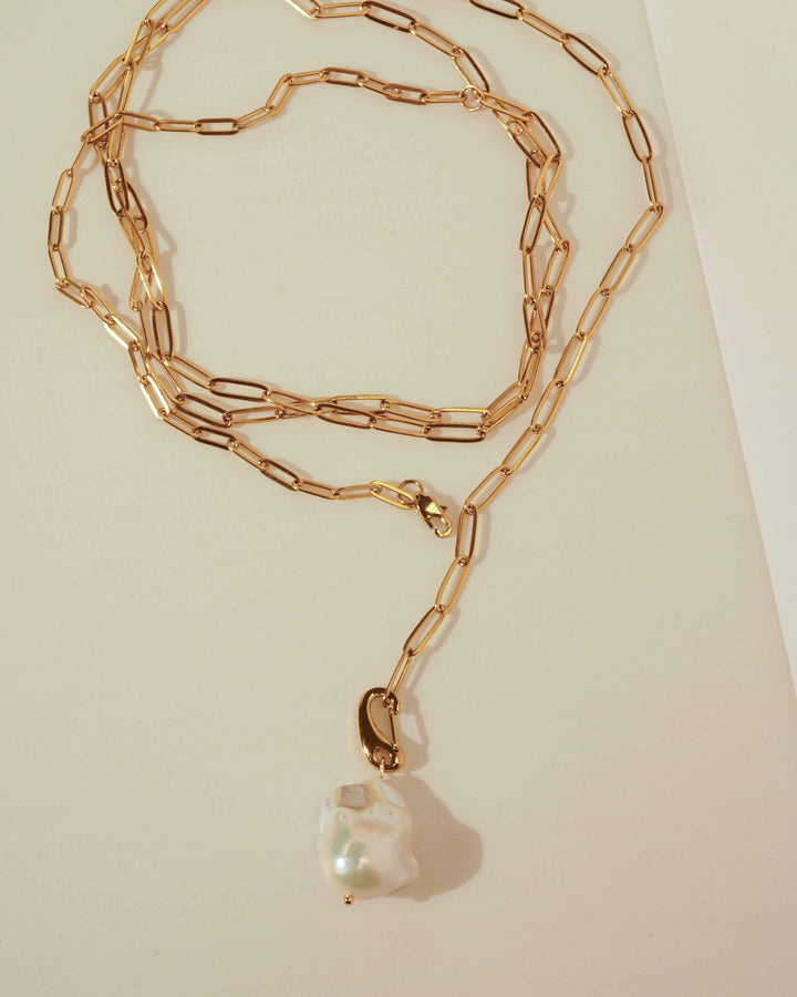 Gold chain necklace with a heart-shaped pearl pendant on a beige background