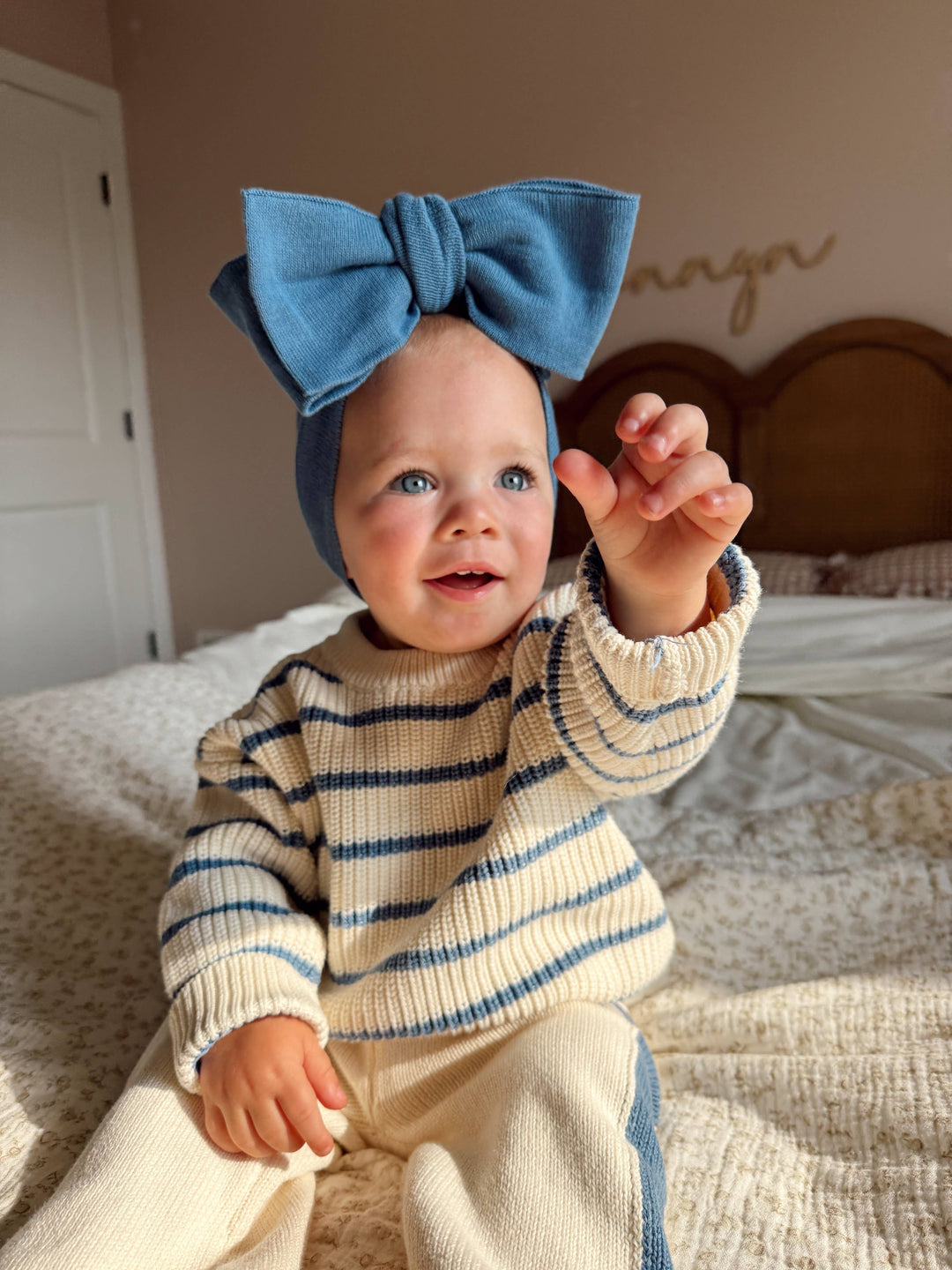 Baby wearing a blue headband with a bow, sitting on a bed.