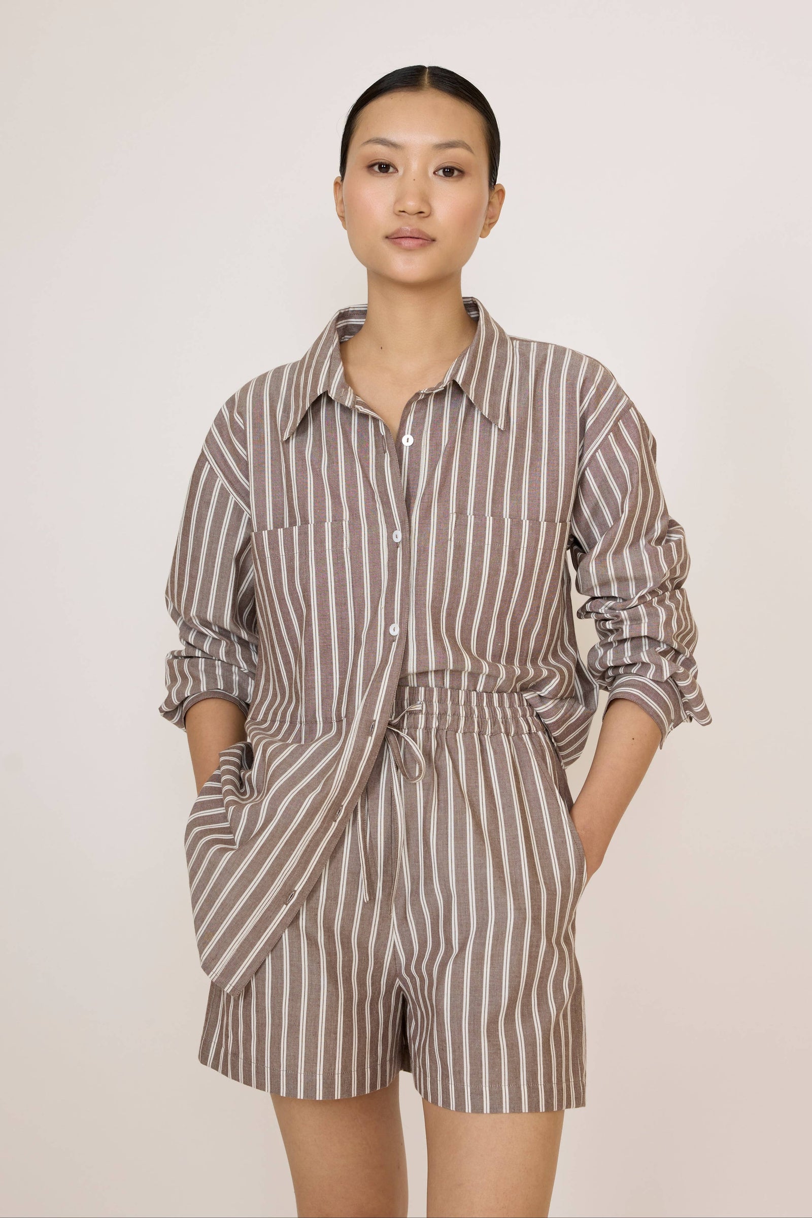 Woman wearing a Laude Everything Shirt in Acorn Stripe and matching shorts set on a plain background