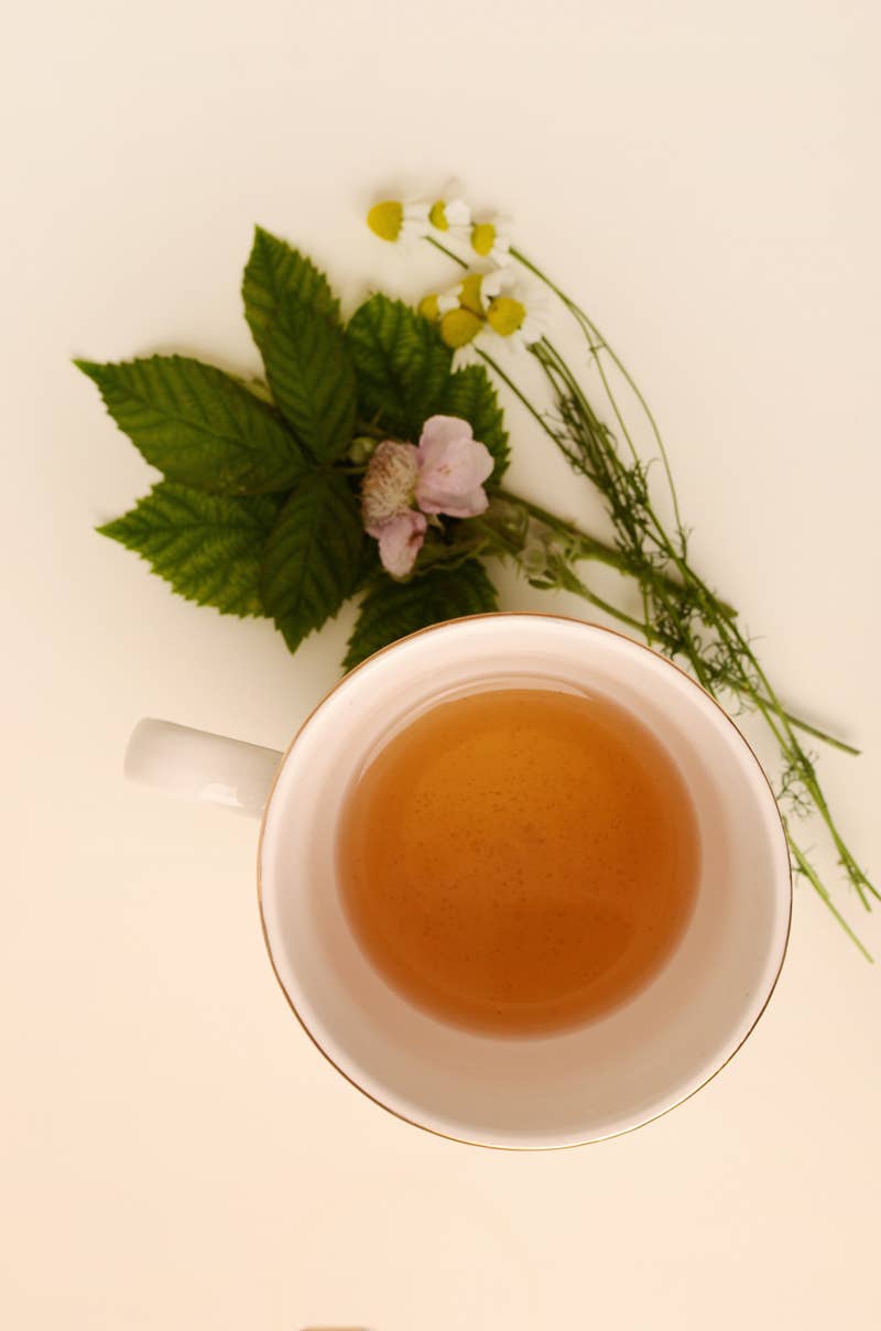 White cup of tea with green leaves and flowers on a light background