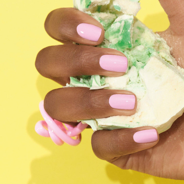Hand with pink nail polish holding a piece of cake against a yellow background