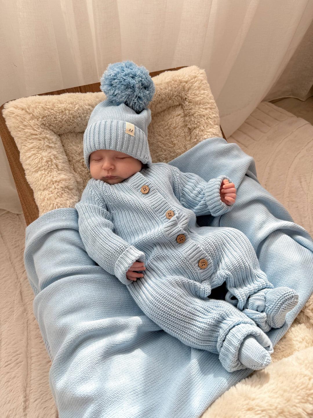 Baby in a light blue knitted outfit and hat lying on a soft surface