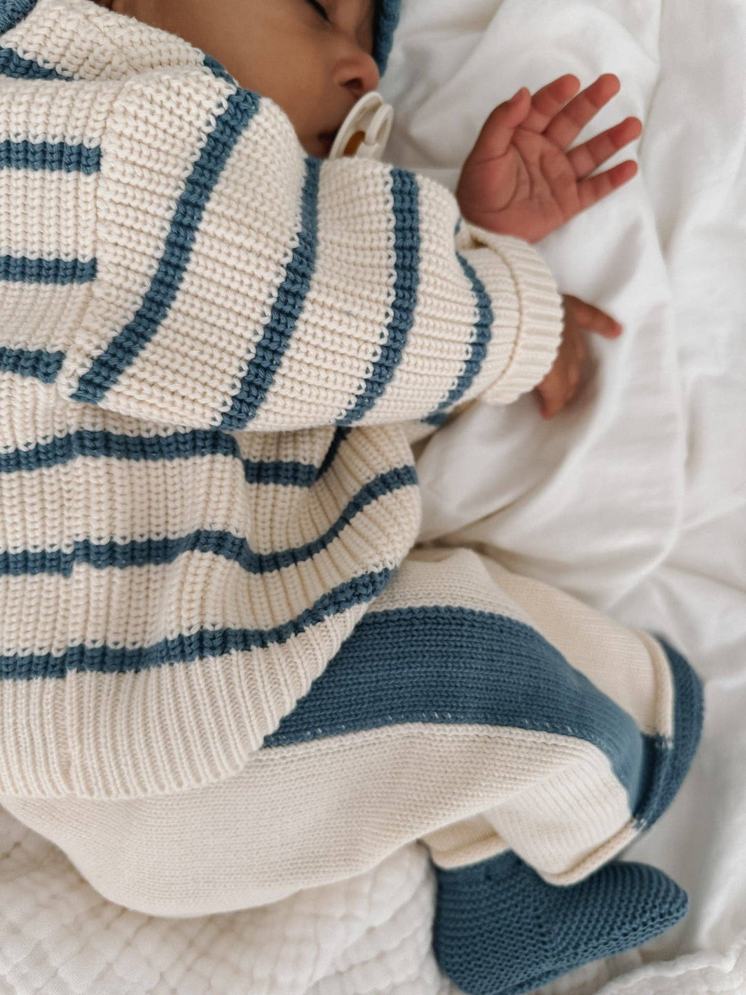 Baby wearing a striped sweater and pants lying on a white blanket