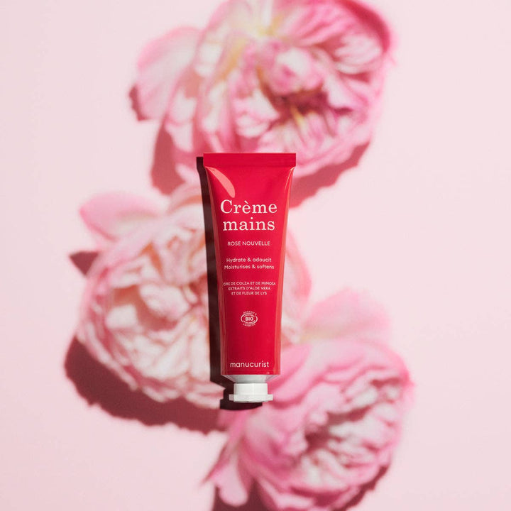 Red hand cream tube labeled 'Crème mains' on pink floral background