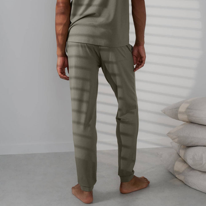 Person wearing olive green pants standing against a white wall with a stack of pillows.