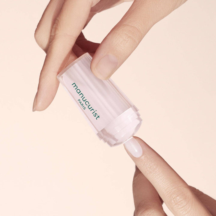 Hand holding a mani stamper to nail against a beige background