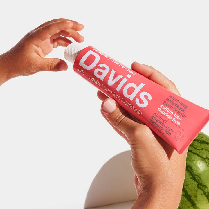Person holding a red 'Davids' toothpaste tube with a white background
