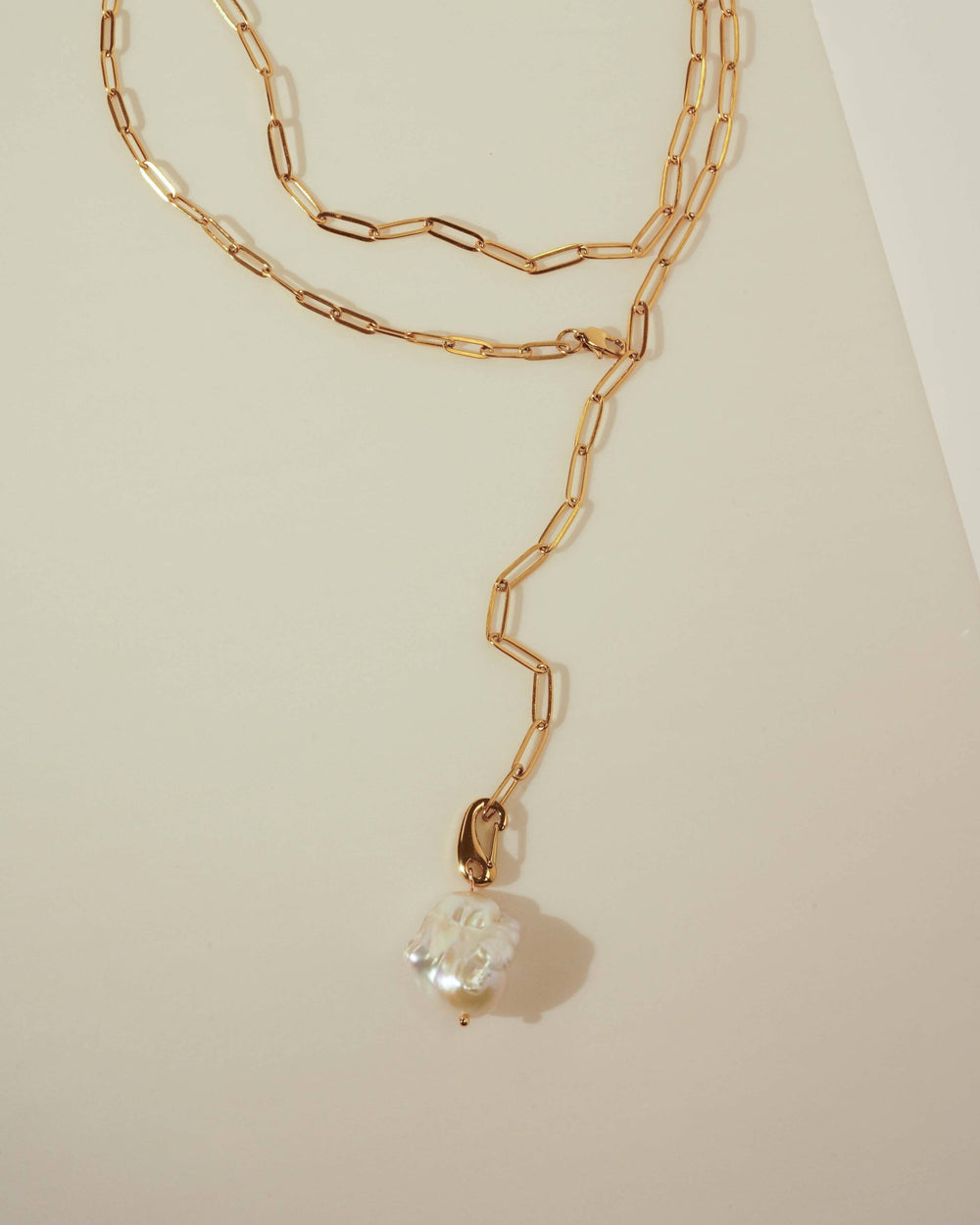 Gold chain necklace with a pearl pendant on a light beige background