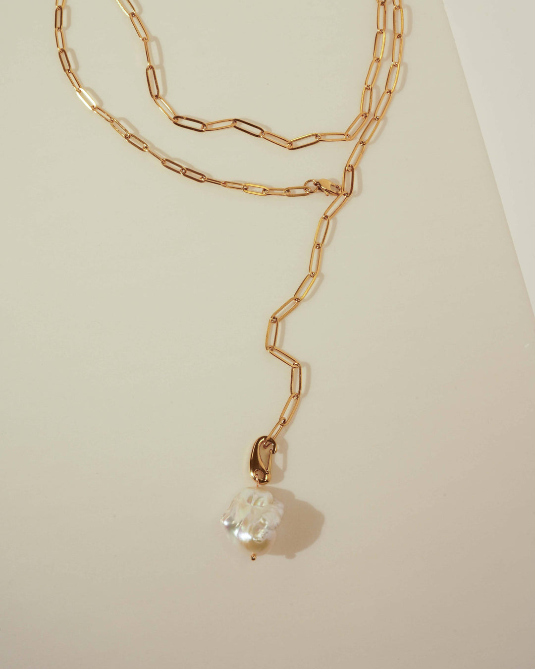 Gold chain necklace with a pearl pendant on a light beige background