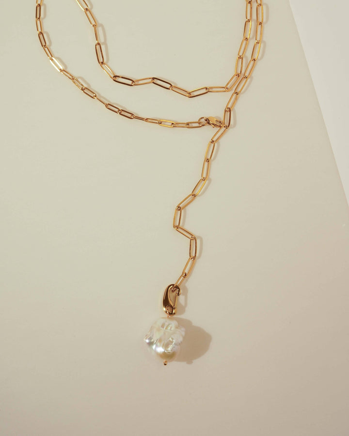 Gold chain necklace with a pearl pendant on a light beige background