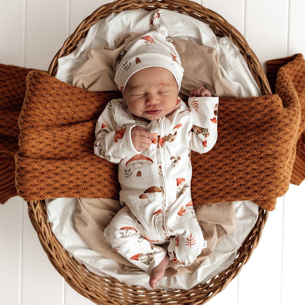 Newborn baby in a wicker basket wearing Snuggle Hunny's Gnomes Organic Snugglesuit Convertible Romper