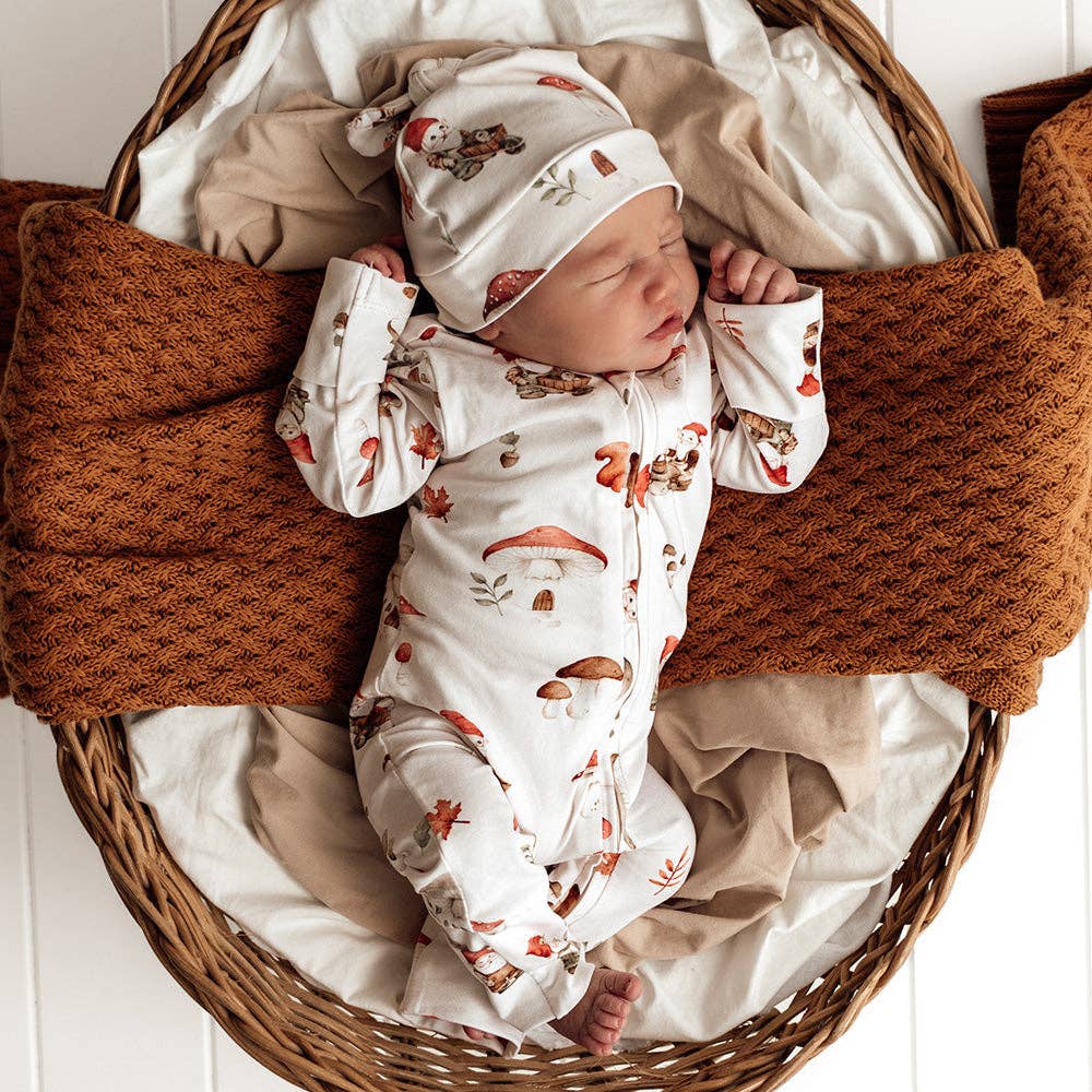 Newborn baby in a wicker basket with brown and beige blankets, wearing a Gnomes Organic Snugglesuit Convertible Romper