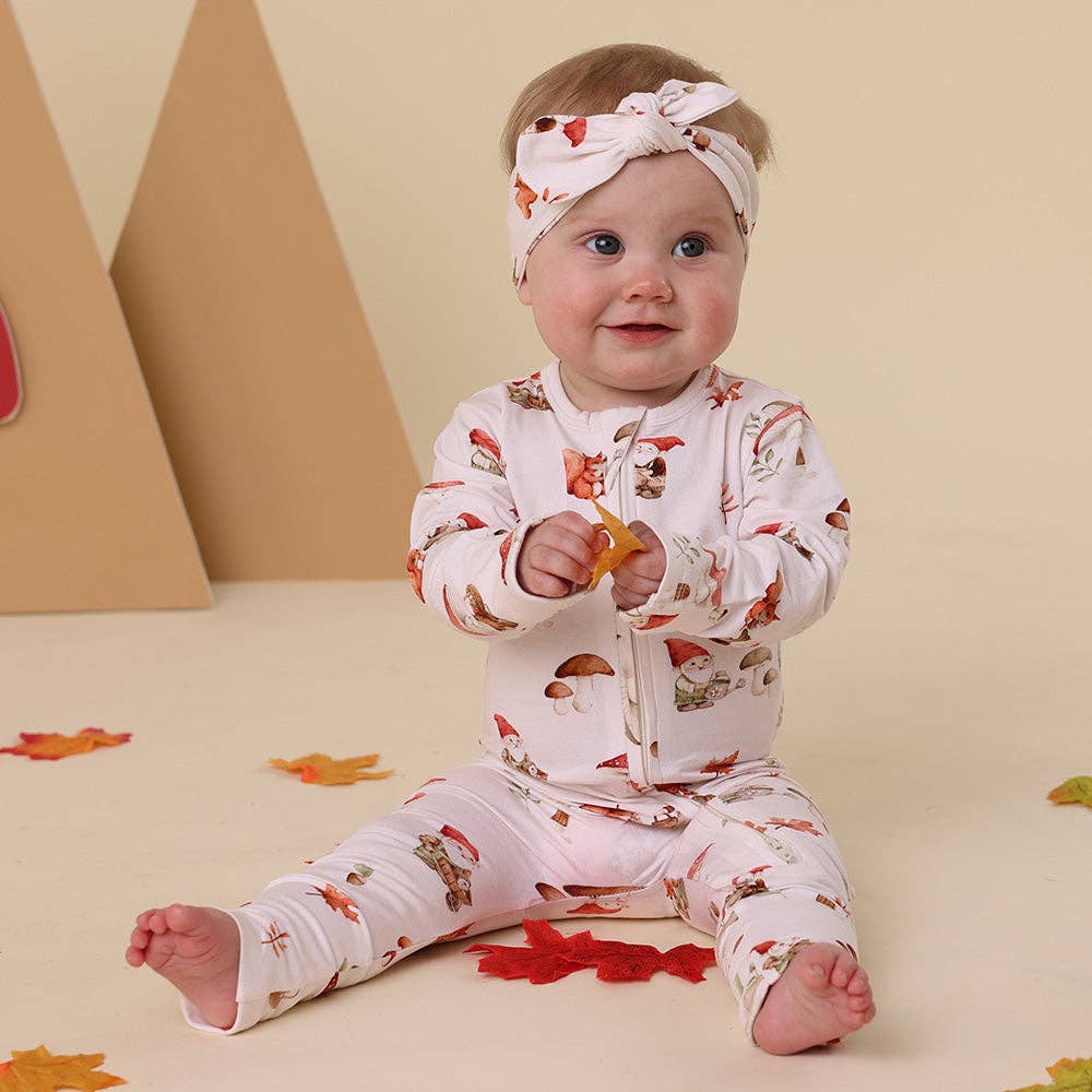 Baby wearing a Gnomes Organic Snugglesuit Convertible Romper, sitting on a beige floor with colorful leaves.