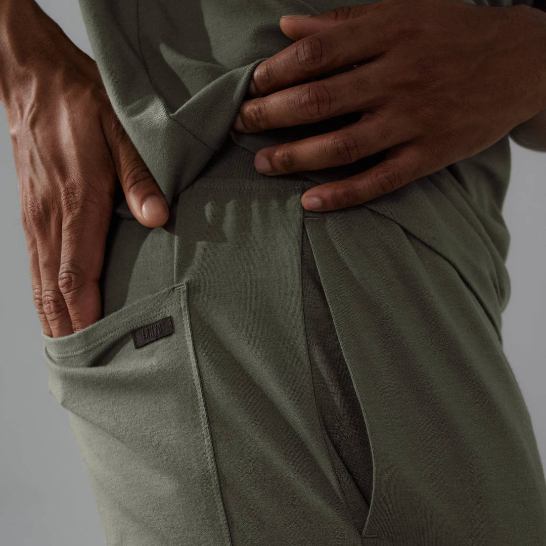 Person wearing olive green pants with a close-up of the waistband on a gray background