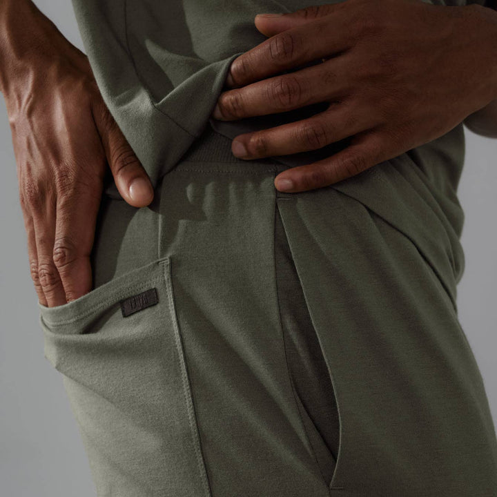 Person wearing olive green pants with a close-up of the waistband on a gray background