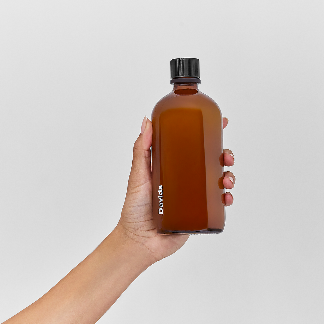 Hand holding a brown Davids bottle with a black cap against a light gray background